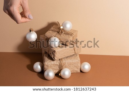 Presents or gift boxes on a beige background with Christmas balls. Girls hand keeping white christmas ball. Holiday decorations. Pepper gift boxes.