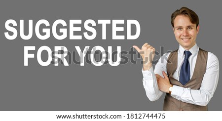Emotional portrait of businessman showing right hand gesture on text - SUGGESTED FOR YOU. Gray background. Business and finance concept