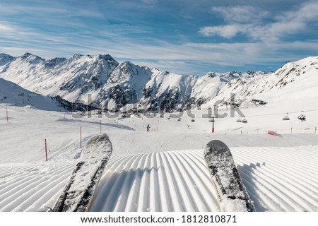 Panorama point of view skier legs on downhill start straight line rows freshly prepared groomed ski slope piste on bright day blue sky background. Snowcapped mountain landscape europe winter resort