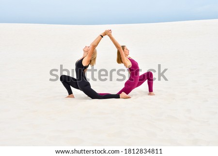 Two beautiful young women performing yoga pose together on the sand