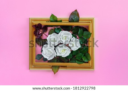 Beautiful white roses with green foliage in vintage wooden frame on bright pink wall for holiday. Creative greeting card.
Copy space for your text.