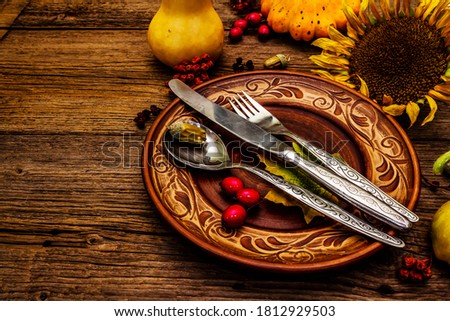 Autumn and Thanksgiving dinner place setting. Harvest of pumpkins and berries, colorful leaves, ceramic plates, fork, spoon, and knife. Fall cutlery wooden background, copy space