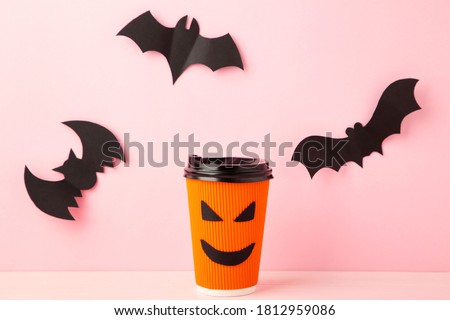 Paper cup with Halloween face in the pink pastel background with halloween bats. Top view