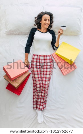 Top view full-length photo of a beautiful young curly brunette woman in casual clothes with shopping bags and credit card in hands. Dreaming about shopping in a mall. Black Friday