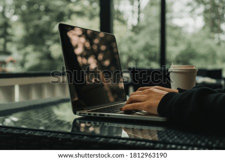 girl sits in a cafe and types on a laptop keyboard. There is a mug of coffee nearby