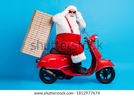 Full length profile side photo of stylish modern white grey hair bearded santa claus drive motor bike deliver x-mas christmas noel pizza stack wear red costume isolated blue color background