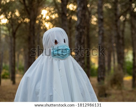 man disguised as ghost with sanitary mask in a forest celebrating halloween during coronavirus pandemic