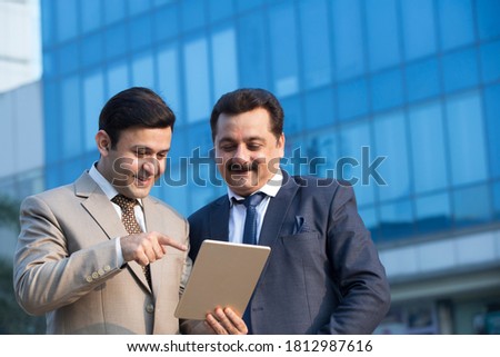 Two Indian businessmen using digital tablet outdoors in city