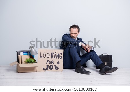 Full length photo of loser worker mature guy jobless handmade placard search work sit floor briefcase belongings box lost success career crash wear suit shoes isolated grey background