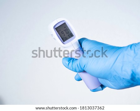 Hand in a blue medical glove keeping the thermometer on a white background. Copy space. Close up. 