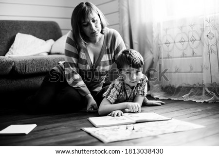 Woman reading a book with her little son on the floor in home. Black and white photo.