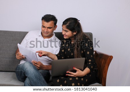 Indian/asian couple accounting, doing home finance and checking bills with laptop while sitting on sofa/couch.