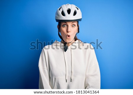 Young beautiful redhead cyclist woman wearing bike helmet over isolated blue background afraid and shocked with surprise expression, fear and excited face.