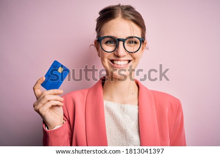 Young beautiful redhead woman holding credit card over isolated pink background with a happy face standing and smiling with a confident smile showing teeth