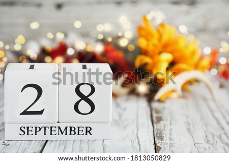 White wood calendar blocks with the date September 28 th and autumn decorations over a wooden table. Selective focus with blurred background. 