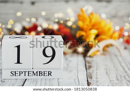 White wood calendar blocks with the date September 19th and autumn decorations over a wooden table. Selective focus with blurred background. 