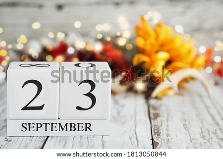 White wood calendar blocks with the date September 23th and autumn decorations over a wooden table. Selective focus with blurred background. 