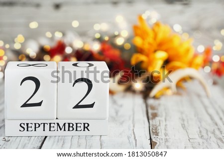 White wood calendar blocks with the date September 22th and autumn decorations over a wooden table. Selective focus with blurred background. 