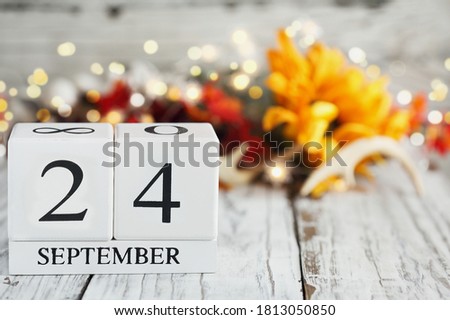 White wood calendar blocks with the date September 24th and autumn decorations over a wooden table. Selective focus with blurred background. 