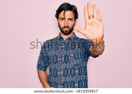 Young handsome hispanic bohemian man wearing hippie style over pink background doing stop sing with palm of the hand. Warning expression with negative and serious gesture on the face.