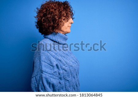 Middle age beautiful curly hair woman wearing casual turtleneck sweater over blue background looking to side, relax profile pose with natural face with confident smile.