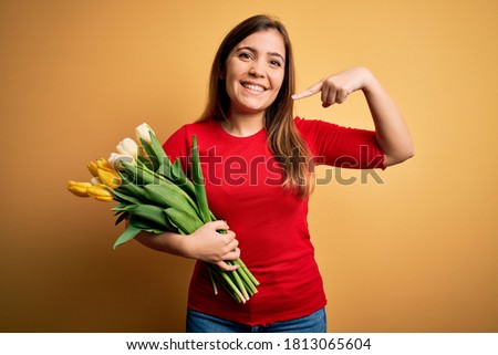 Young blonde woman holding romantic bouquet of tulips flowers over yellow background smiling cheerful showing and pointing with fingers teeth and mouth. Dental health concept.
