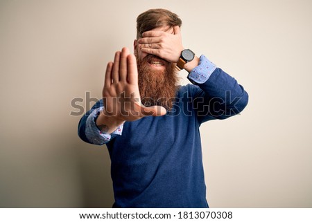Handsome Irish redhead business man with beard standing over isolated background covering eyes with hands and doing stop gesture with sad and fear expression. Embarrassed and negative concept.