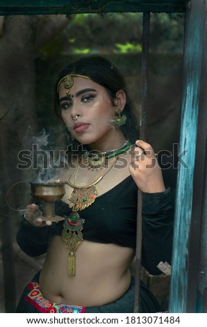 Portrait of a Rajasthani lady holding Indian frankincense or Dhunuchi, coming out from the window, Wearing a black traditional Rajasthani lehenga dress with oxidized jewelry, holding incense burner
