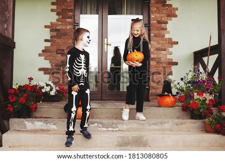 Brother and sister celebrate halloween on the street near the house in costumes and make-up with a pumpkin lantern,