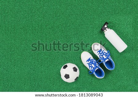 Soccer ball, cleats and water bottle on green artificial turf, top view with copy space, football concept. Game or sports club class and tournament concept