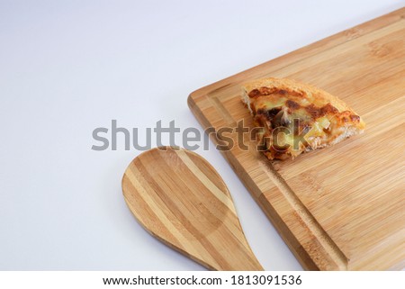 Slice of pizza on wooden chopping board and wooden spoon on white background