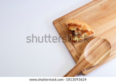 View from above of slice of pizza and wooden spoon on wooden chopping board on white background 