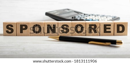 SPONSORED written on wooden cubes near a calculator and a pen on a light background. Investment concept