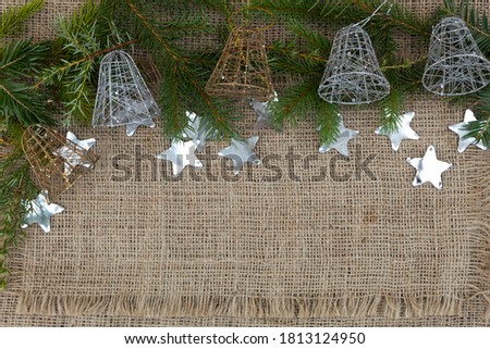 Spruce branches and five New Year's bells lie on the jute fabric. Nearby lies confetti in the form of stars.