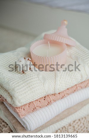 A stack of knitted sweaters, cotton, a candle. Women's sweaters are on the ottoman. Cozy autumn clothes. Fall.