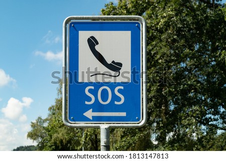 emergency phone sign painted with black phone on white-blue background against blue sky and green forest, emergency calls are important to save lives, by day