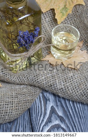 A bottle of lavender tincture. A bouquet of lavender is tied to the bottle. Nearby is a glass of drink and dried maple leaves. On coarse linen. Close-up shot.