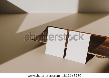 Blank paper sheet cards with mockup copy space and wooden tray with sunlight shadow on beige table. Minimal business brand template