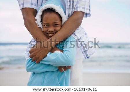 Close-up of daughter being hugged by the father standing behind on beach.