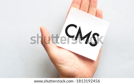 Businessman's hand in a pink shirt sleeve holding paper business card with text CMS, closeup isolated over white background