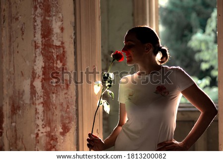 Silhouette of a young woman smelling a red rose in a ruined, abandoned house. Happiness. Good times - bad times concept. Backlight.