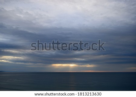 Dramatic and intense clouds over the sea with rays of sunset light Royalty-Free Stock Photo #1813213630