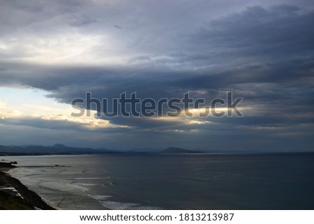 View of the coast and the sea with stormy clouds and mountains in the distance at sunset time