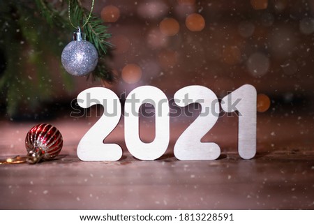 Wooden numbers 2021.New Year magic background with bokeh, falling snow, spruce branch and christmas balls. Christmas decoration with white number. Winter holiday greeting card template.