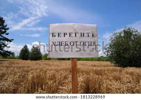 a sign with the inscription in Russian Take care of the bread from the fire  in the middle of a wheat field harvest cereals autumn time