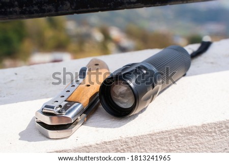 Folding knife and flashlight lying on the concrete fence. Tourist equipment, trekking, hiking and camping activity concept. Stock photo.