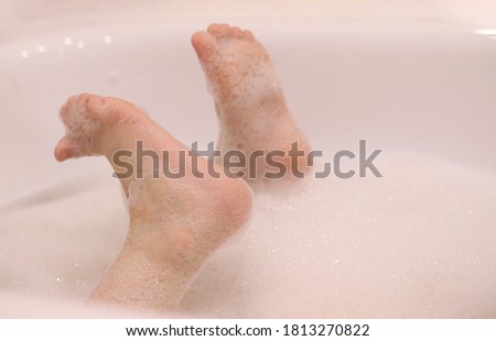 Caucasian children's feet in foam. Baby takes a bath. Hygienic procedure.