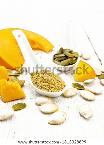 Flour and pumpkin seeds in white spoons, slices of vegetable on a wooden board background