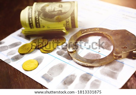 Economic crime concept.Roll of banknotes with judge gavel and police handcuff on police fingerprint crime page file.