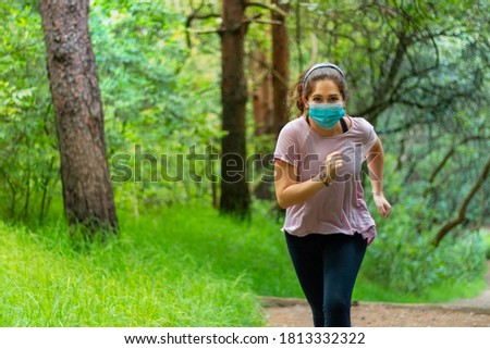 Real woman running in a forest, wearing face mask to avoid contagion of coronavirus. New Normal